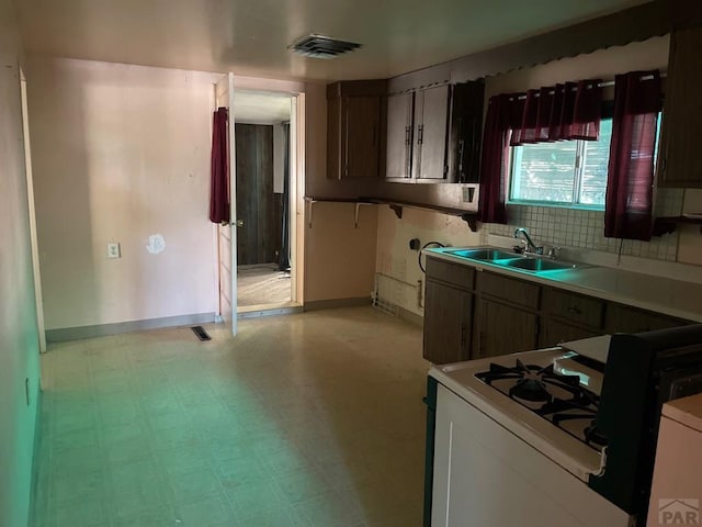 kitchen with white gas stove, light floors, light countertops, visible vents, and a sink