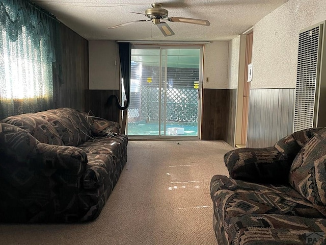 carpeted living area with a ceiling fan, wainscoting, wood walls, and a textured ceiling