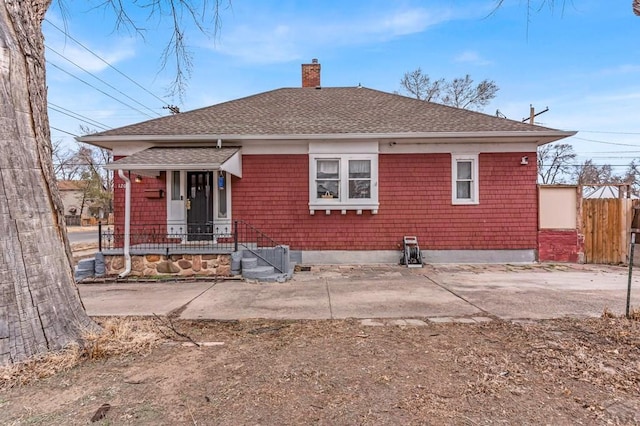 rear view of property featuring a chimney, fence, and roof with shingles