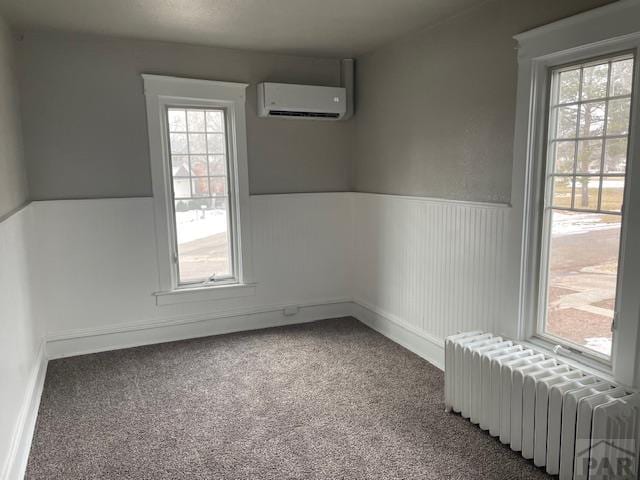 unfurnished room with a wall unit AC, wainscoting, carpet flooring, and radiator