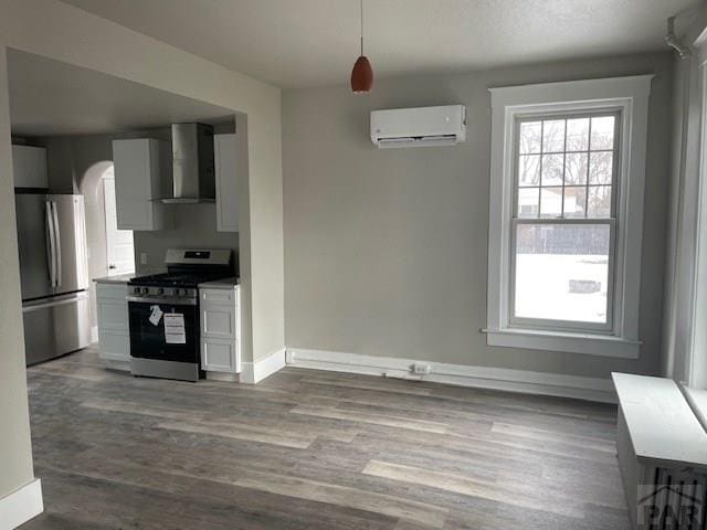 kitchen with dark wood finished floors, a wall mounted air conditioner, stainless steel appliances, light countertops, and wall chimney range hood