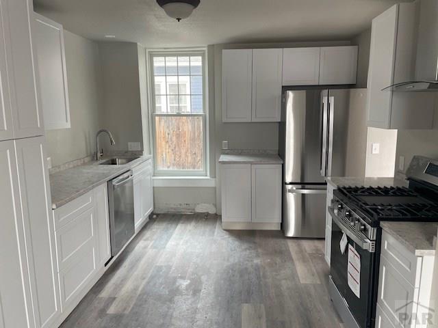 kitchen featuring stainless steel appliances, white cabinetry, a sink, and wall chimney range hood