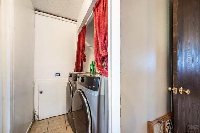 washroom featuring laundry area, washing machine and dryer, light tile patterned floors, and a textured ceiling