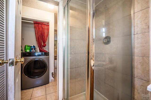 bathroom with tile patterned flooring, a shower stall, and washer / dryer