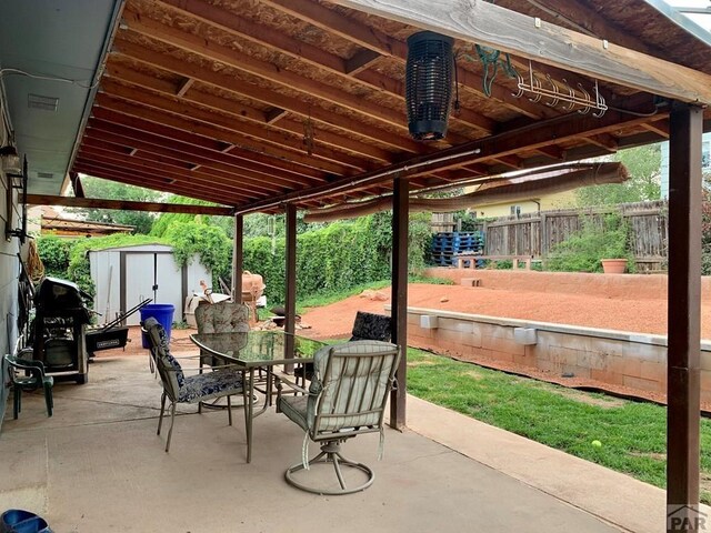 view of patio / terrace featuring an outbuilding, outdoor dining area, fence, and a storage shed