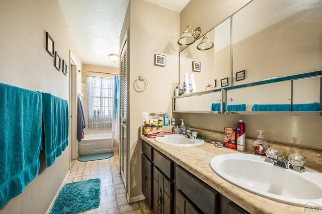 full bathroom featuring baseboards, a sink, a bath, and double vanity