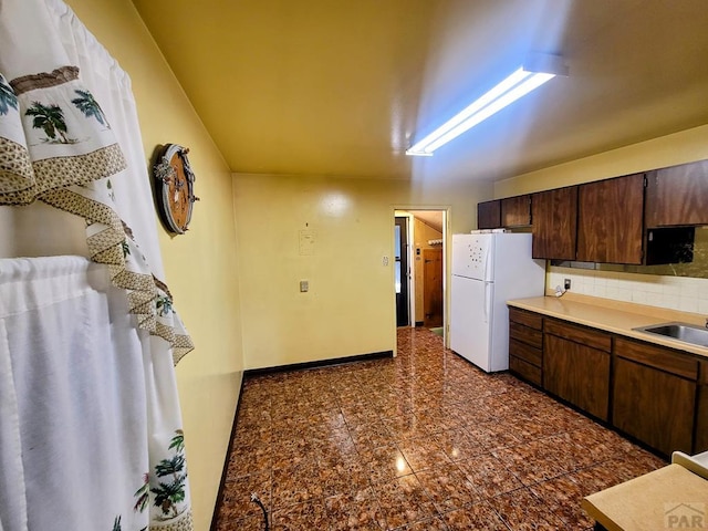 kitchen featuring a sink, granite finish floor, freestanding refrigerator, dark brown cabinetry, and decorative backsplash