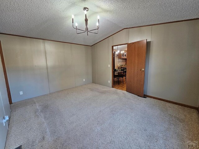 carpeted spare room featuring vaulted ceiling, a textured ceiling, and a chandelier