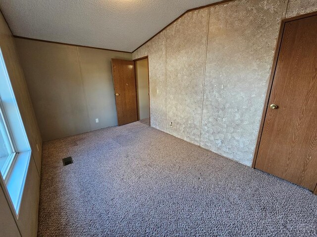 carpeted spare room with lofted ceiling, crown molding, visible vents, and a textured ceiling