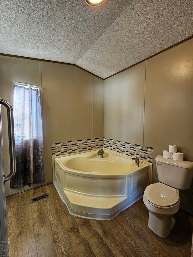 bathroom with a textured ceiling, wood finished floors, visible vents, vaulted ceiling, and a bath