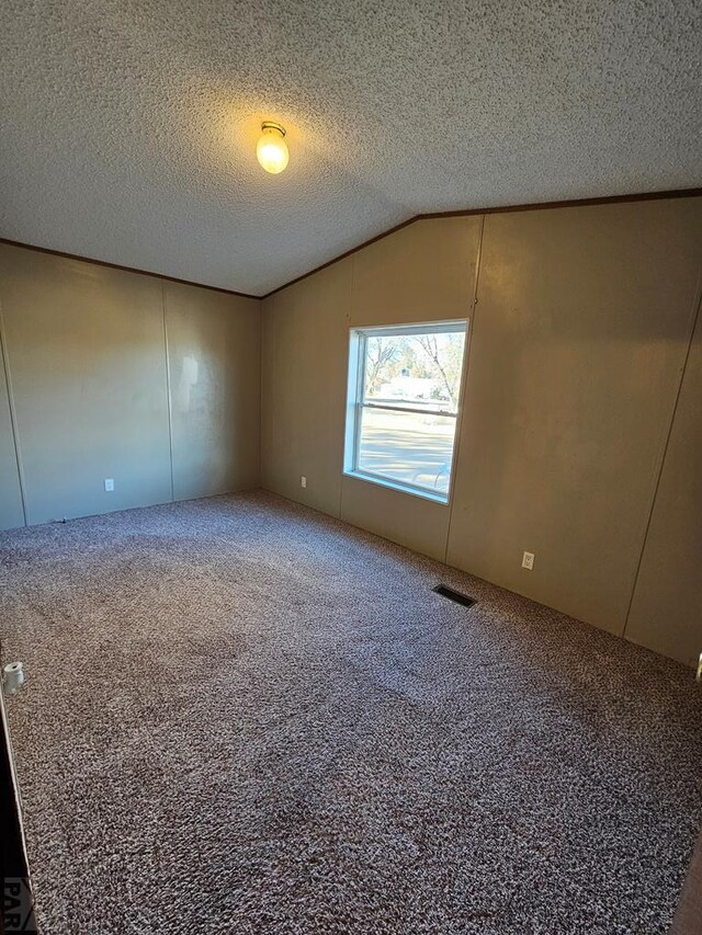 spare room with carpet floors, visible vents, vaulted ceiling, and a textured ceiling