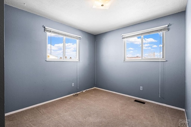 carpeted spare room featuring a textured ceiling, plenty of natural light, visible vents, and baseboards