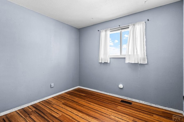 spare room featuring wood finished floors, visible vents, and baseboards