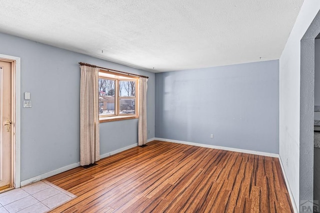 empty room featuring a textured ceiling, light wood-style flooring, and baseboards