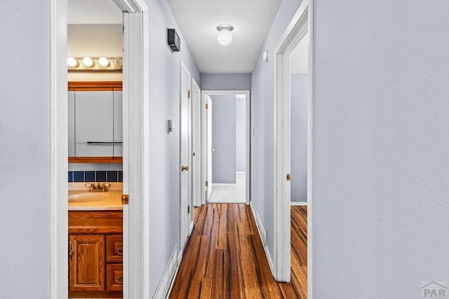 corridor with dark wood-style flooring, a sink, and baseboards