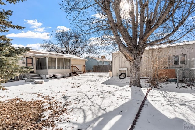 snowy yard with entry steps, a sunroom, and fence