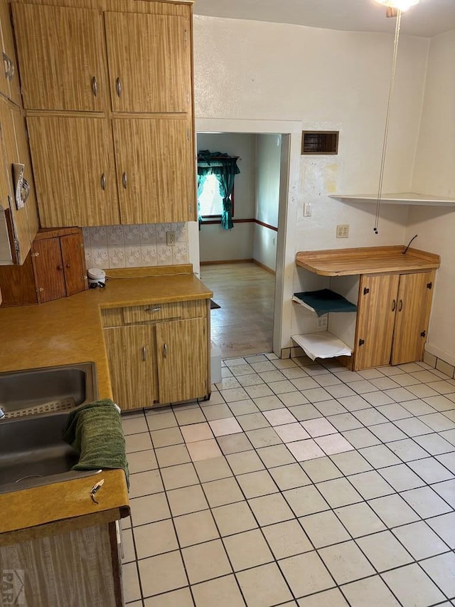 kitchen with brown cabinetry, light countertops, visible vents, and light tile patterned flooring