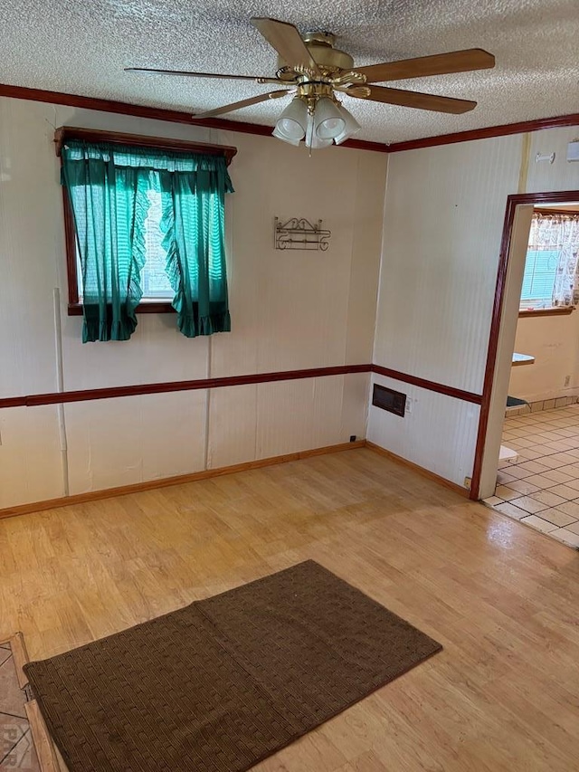 unfurnished room featuring light wood-style floors, a ceiling fan, ornamental molding, and a textured ceiling