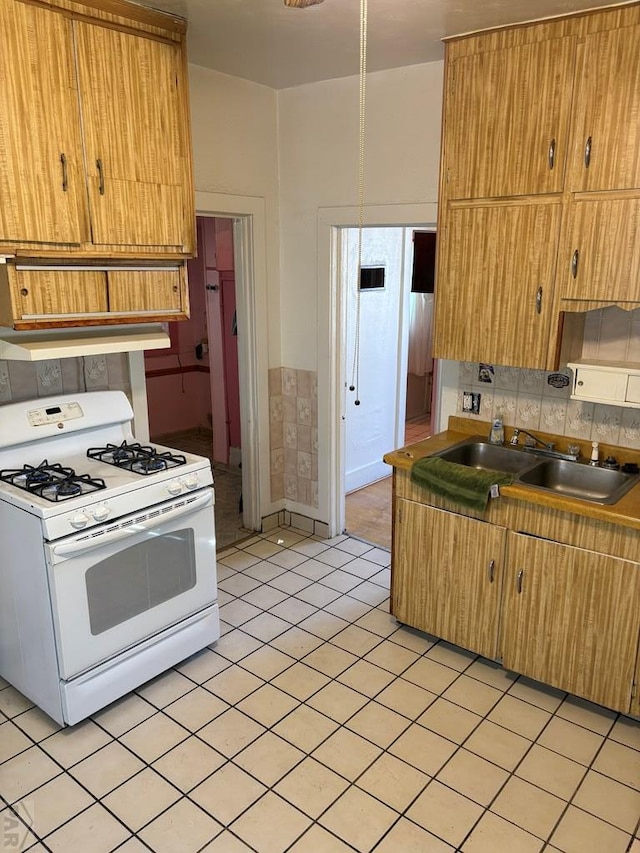 kitchen featuring gas range gas stove, a sink, backsplash, and brown cabinets