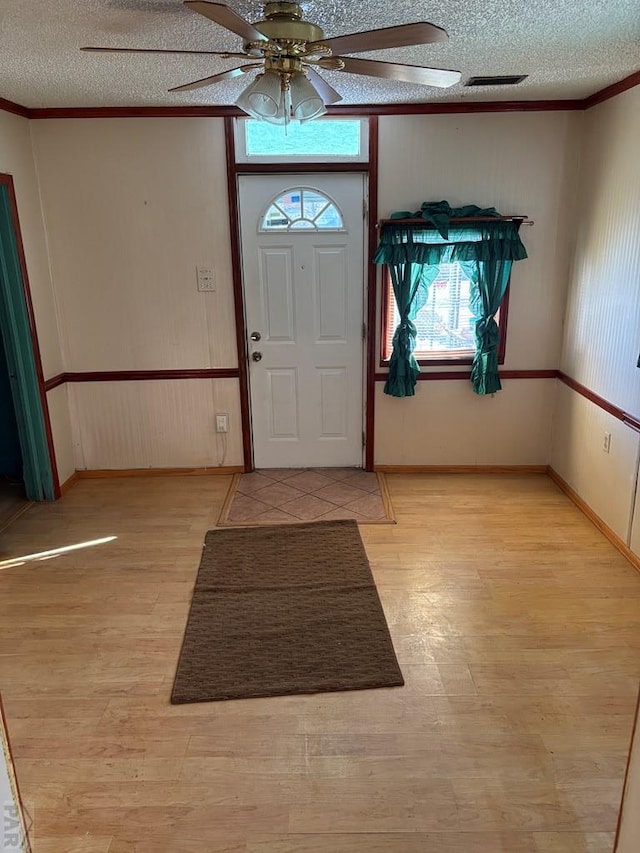 foyer entrance featuring crown molding, light wood finished floors, visible vents, ceiling fan, and a textured ceiling