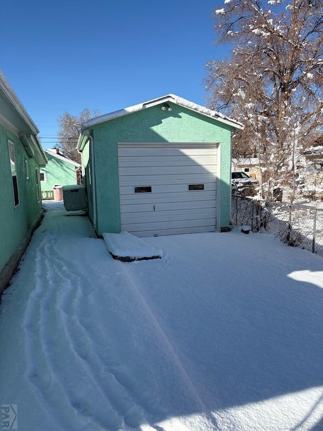 snow covered garage featuring a garage and fence