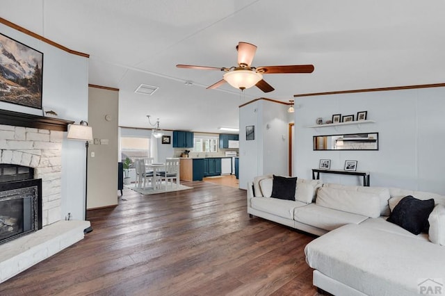 living room featuring ceiling fan, dark wood-type flooring, ornamental molding, a stone fireplace, and visible vents