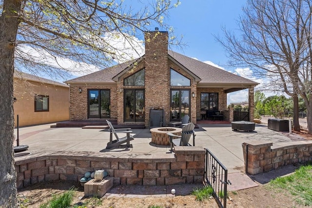 rear view of property with a chimney, a patio area, roof with shingles, an outdoor fire pit, and brick siding