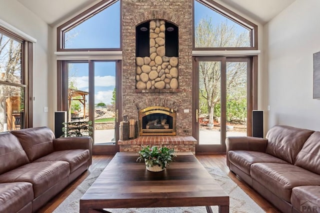 living area featuring hardwood / wood-style floors, high vaulted ceiling, a healthy amount of sunlight, and a brick fireplace