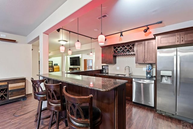 kitchen with dark wood finished floors, dark stone countertops, appliances with stainless steel finishes, a sink, and a kitchen breakfast bar