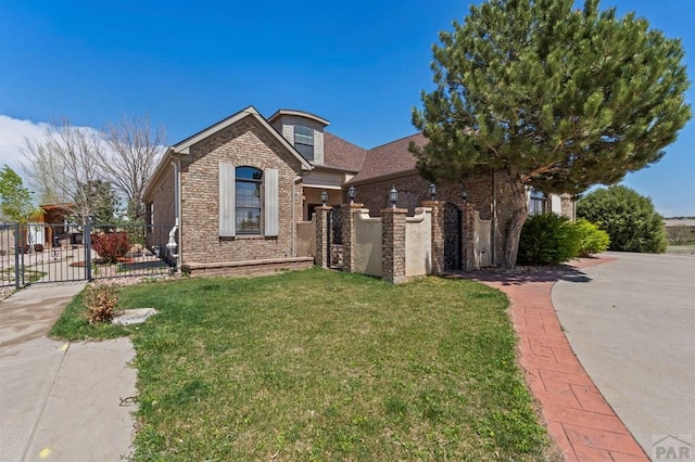 view of front of home with a gate, brick siding, fence, and a front lawn