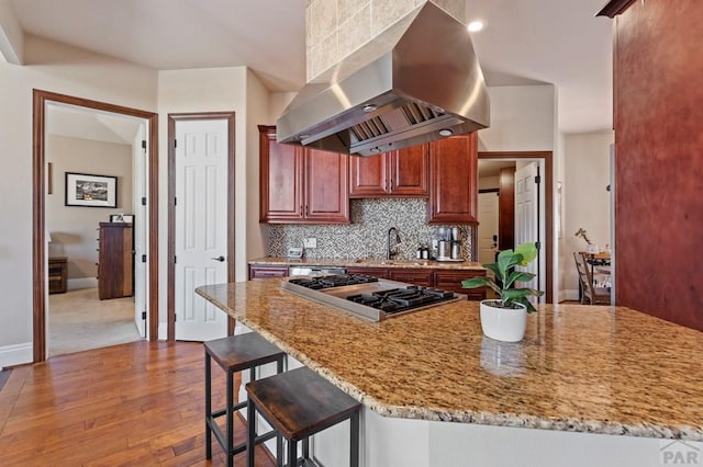 kitchen with a kitchen bar, light stone counters, backsplash, hardwood / wood-style floors, and island range hood