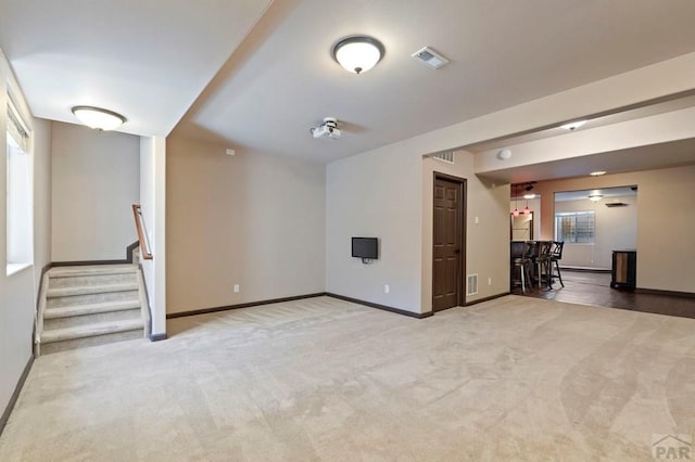 unfurnished living room featuring stairs, visible vents, light colored carpet, and baseboards