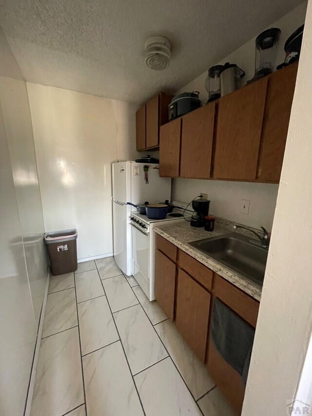 kitchen with a textured ceiling, a sink, light countertops, brown cabinetry, and white electric range oven