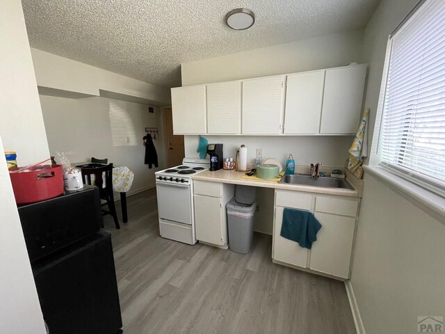 kitchen with white electric range, a sink, white cabinetry, light countertops, and light wood-type flooring