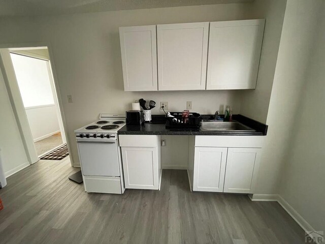 kitchen with electric stove, light wood finished floors, dark countertops, white cabinetry, and a sink