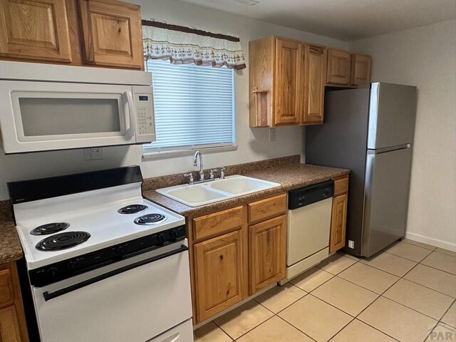 kitchen featuring white appliances, light tile patterned floors, brown cabinetry, dark countertops, and a sink