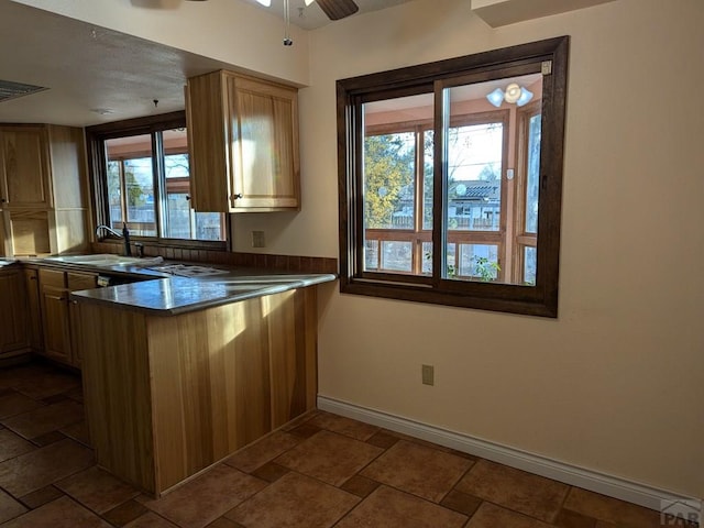 kitchen with stone tile floors, baseboards, dark countertops, a peninsula, and a sink