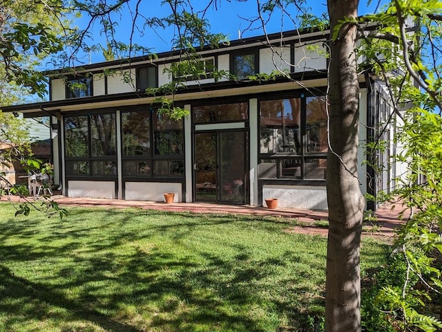 back of property featuring a yard, a sunroom, and stucco siding