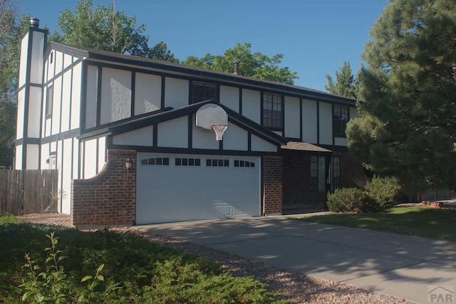 tudor home featuring brick siding, concrete driveway, a chimney, an attached garage, and stucco siding