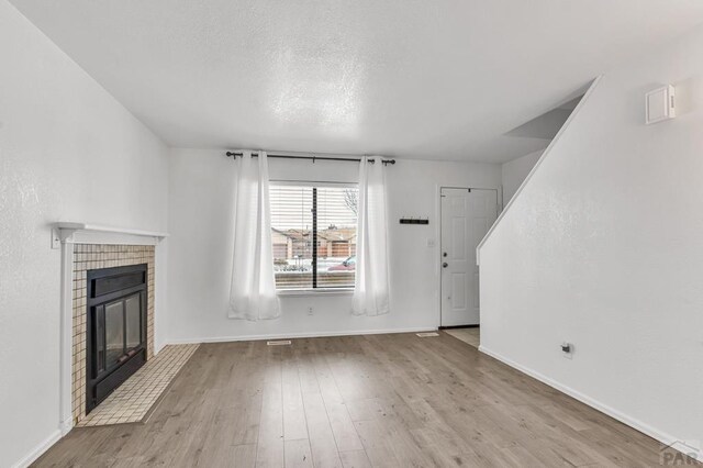 unfurnished living room featuring a textured ceiling, a tile fireplace, light wood-style flooring, and baseboards