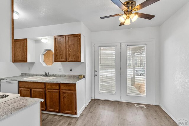 kitchen featuring light wood finished floors, light countertops, brown cabinetry, white dishwasher, and a sink