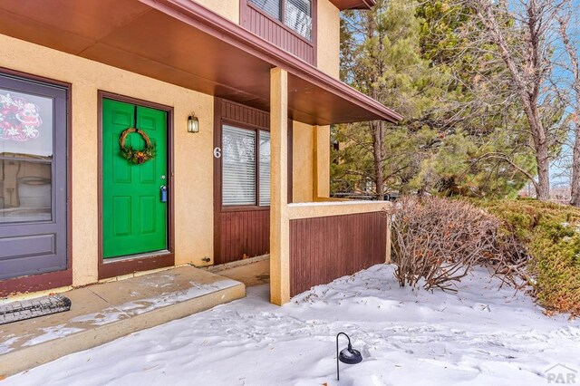 snow covered property entrance with stucco siding