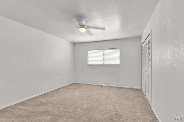 unfurnished bedroom featuring a textured ceiling, baseboards, a closet, and light colored carpet