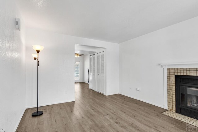 unfurnished living room with a ceiling fan, baseboards, wood finished floors, and a tile fireplace