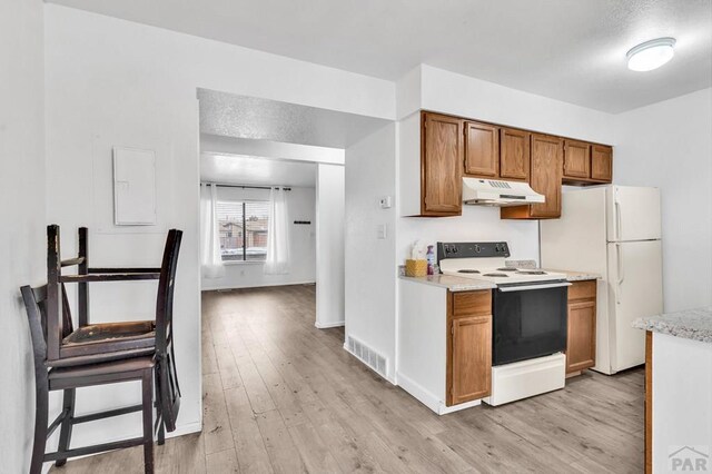 kitchen featuring white appliances, brown cabinetry, light wood-style flooring, light countertops, and under cabinet range hood