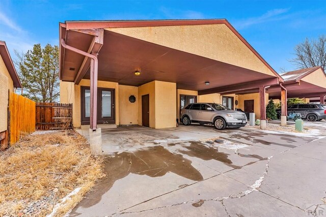 view of front of property featuring driveway, an attached carport, fence, and stucco siding