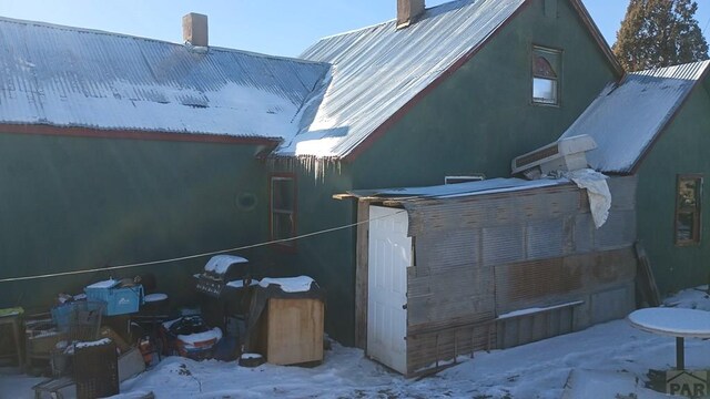 snow covered property featuring a chimney, metal roof, and stucco siding