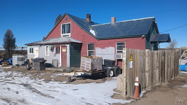 snow covered back of property featuring fence and metal roof