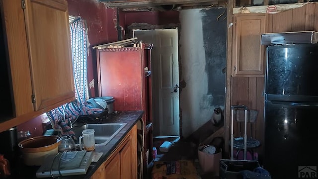 kitchen with dark countertops, a sink, freestanding refrigerator, and brown cabinets