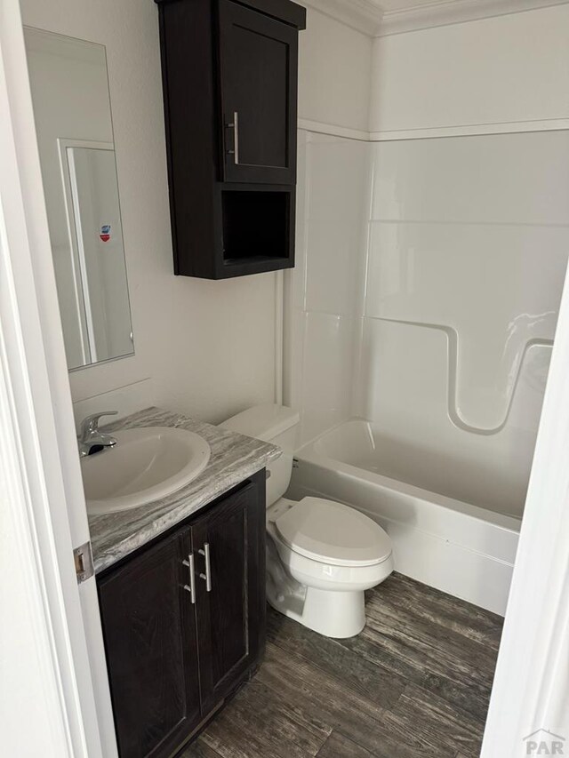 bathroom with crown molding, toilet, vanity, wood finished floors, and  shower combination